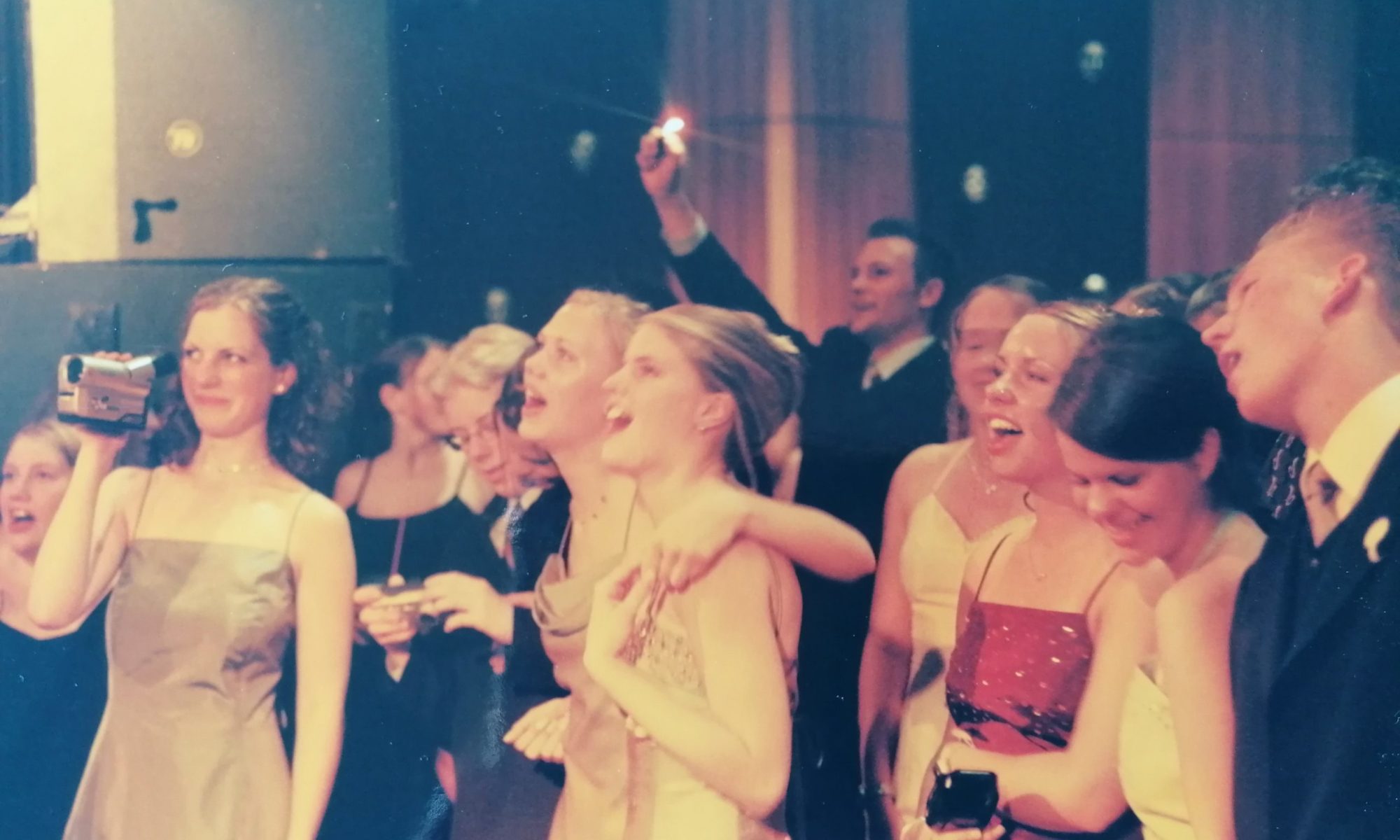 Abiball: Absolventinnen und Absolventen singen und filmen, im Hintergrund eine Wunderkerze